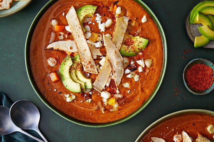 Hominy white corn, Guajillo chilli and tortilla soup with queso fresco A bowl of red Mexican soup topped with tortilla strips