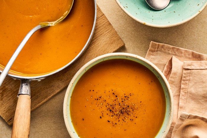 Sweet potato soup A pan and bowl of sweet potato soup next to an empty bowl with spoons