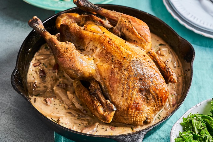 Roast guinea fowl with shallots, lardons and white wine A black baking dish filled with a roast bird on a bed of creamy sauce