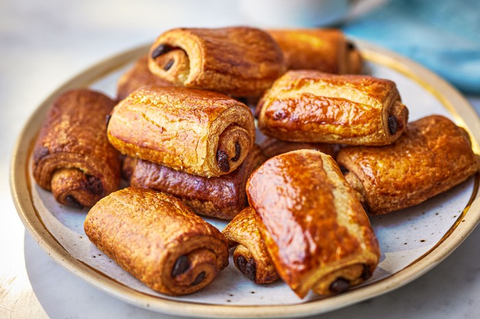 Pain Au Chocolat Recipe A plate of pain au chocolats with a mug of tea behind