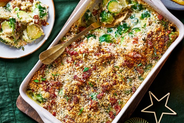 Brussels Sprout Gratin A brussels sprout and bacon gratin in a large white baking dish, next to a plate of parsnips