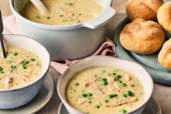 Chicken soup A pot and two bowls of chicken soup next to a board of bread rolls
