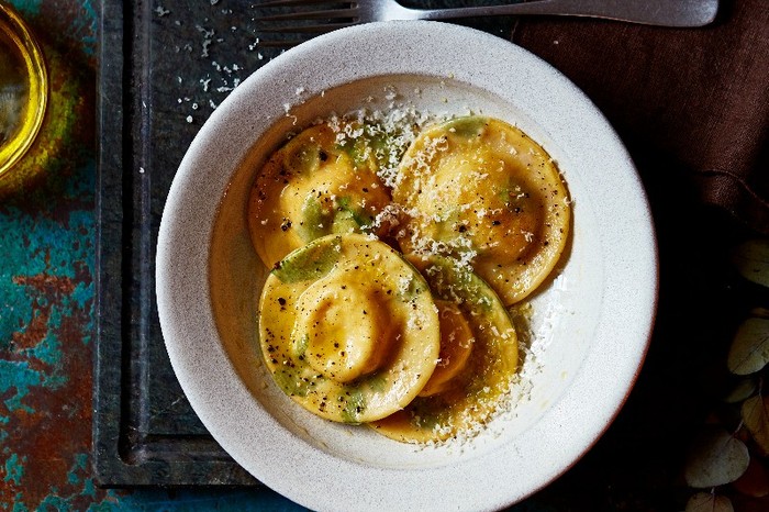 Classic homemade ravioli A white bowl of fresh ravioli on a black board with a fork