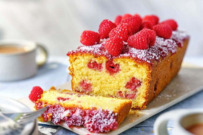 A raspberry loaf cake with berries on top and one slice taken out of it