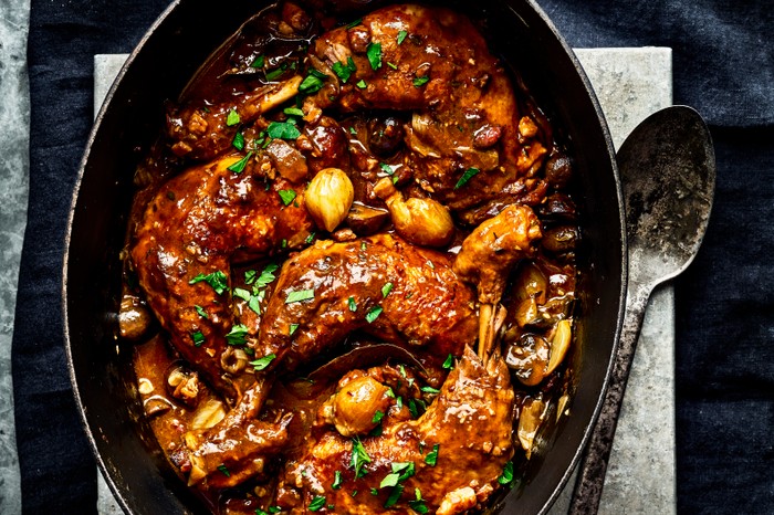 Coq au vin A black oval casserole pot with a serving spoon, filled with coq au vin and topped with parsley