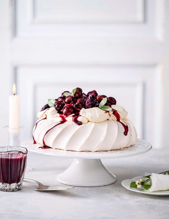 Mulled wine cherry pavlova on a cake stand with a white background