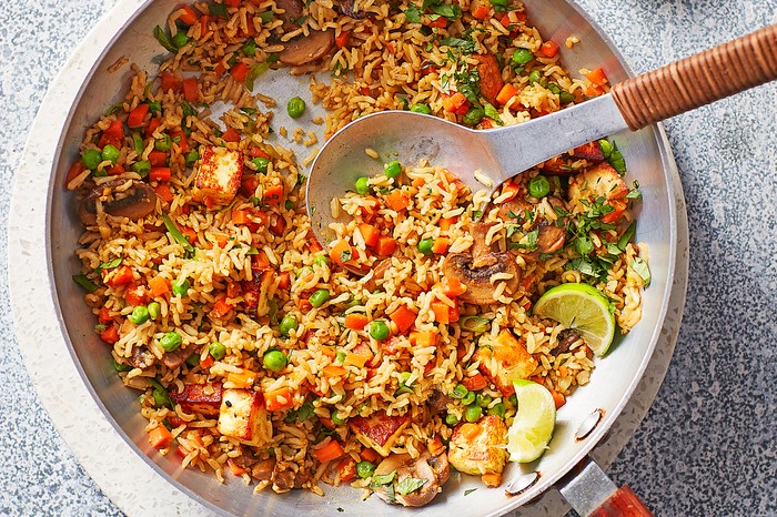 Healthy fried rice A silver pan of rice with vegetables with a serving spoon on a stone board next to wedges of lime