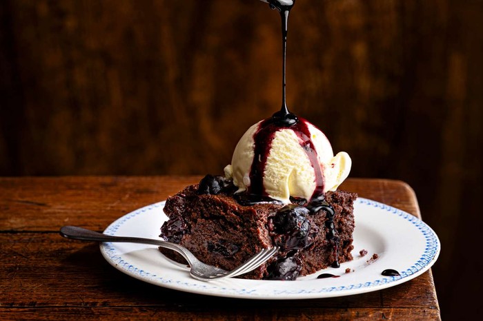 A single chocolate brownie with ice cream and chocolate sauce on top