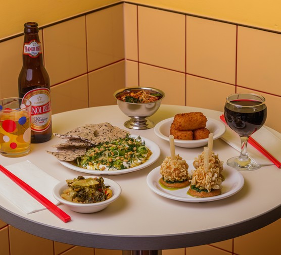 Lai Rai, Peckham A selection of small plates, beer and wine on a bar table, with a butter yellow tiled wall in the background