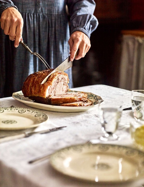 Someone carving roast pork on a set table