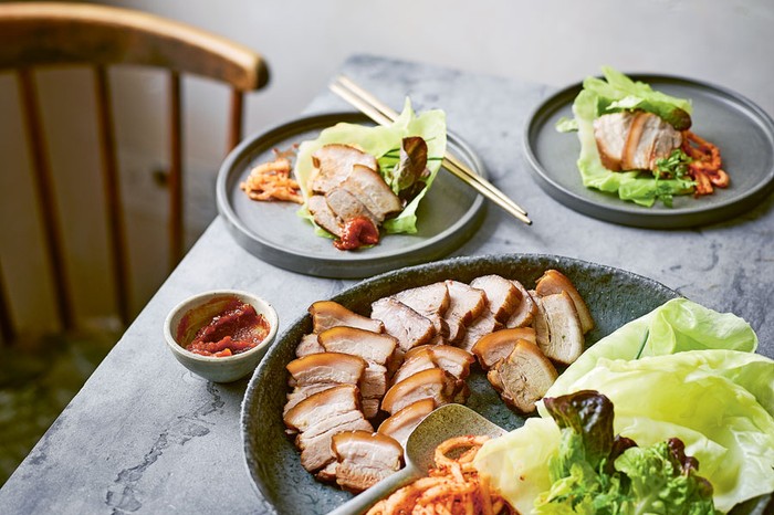 Korean bossam (pork-belly) wrap A large plate and two smaller plates of pork belly, radish salad and lettuce leaves next to a ramekin of sauce
