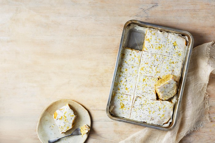 Lemon, olive oil and chia sheet cake A frosted sheet cake with one slice taken out of it