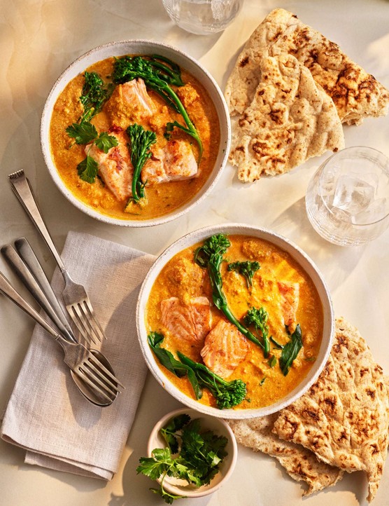 Two bowls of salmon curry with cutlery on the side