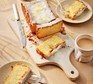Gluten-free lemon drizzle cake A lemon loaf cake with one slice cut off and cups of tea on the side