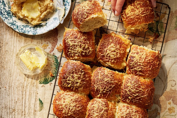 A batch of fresh cheese-topped rolls on a cooling rack