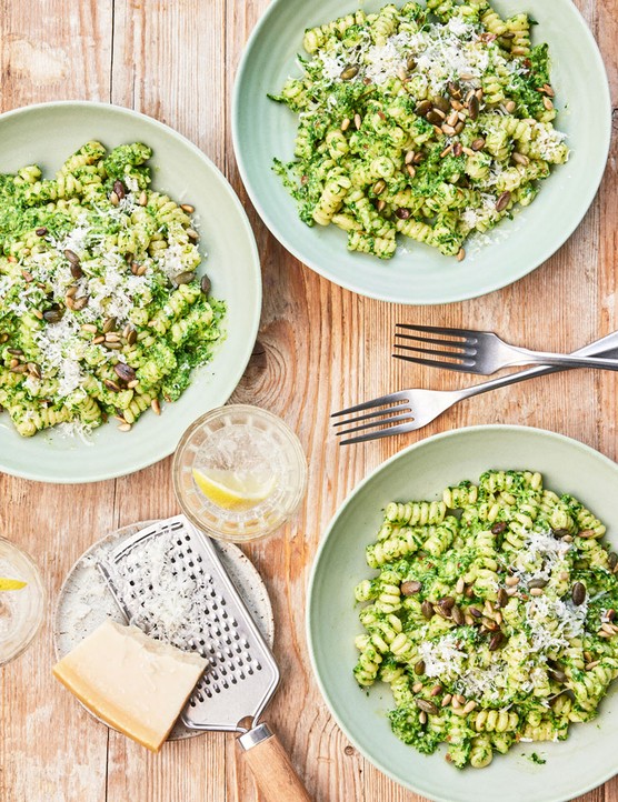 Three bowls of green pasta topped with pumpkin and sunflower seeds