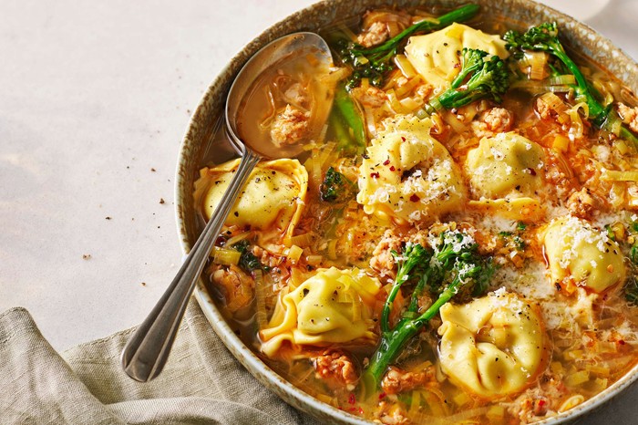 Smoky sausage and greens tortellini broth A large bowl of tortellini soup with a spoon in it
