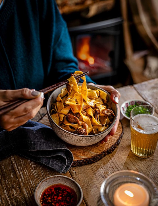 A bowl of mushroom pasta with a glass of beer on the side