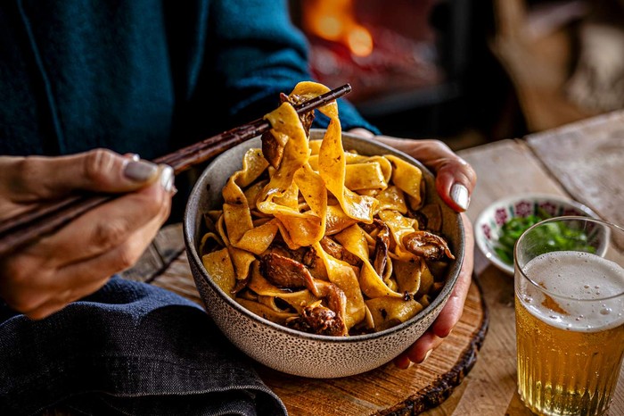 A bowl of mushroom pasta with a glass of beer on the side