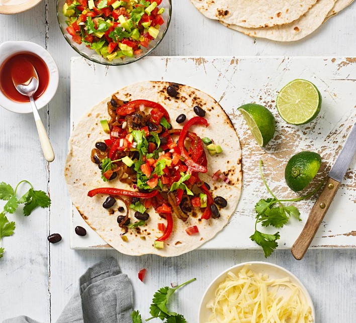 Easy Vegetable Fajitas Recipe Veggie fajitas with beans, peppers, avocado, coriander and lime, on a chopping board with lime wedges and a knife