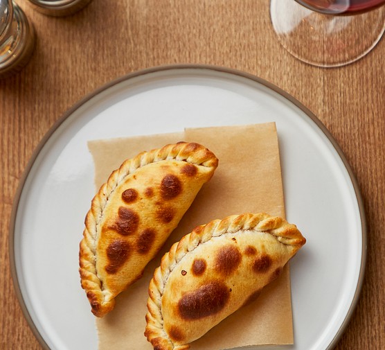 A white plate topped with two empanadas with crimped pastry