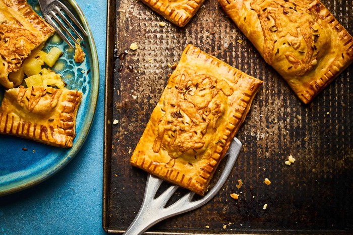 Cumin spiced swede and gouda pasties Fresh golden pasties on a cooling sheet