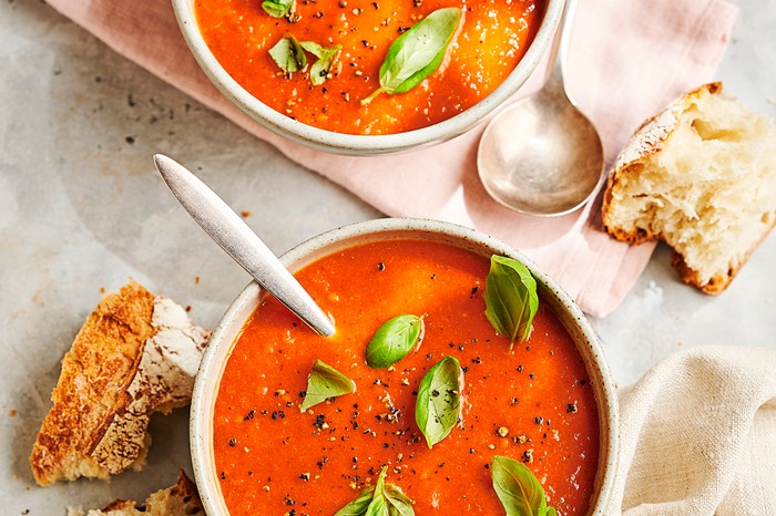 Tomato and red pepper soup two bowls of red soup scattered with basil leaves and sat on folded linen napkins with chinks of crusty bread