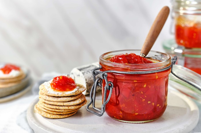 A jar of tomato jam with a stack of crackers next to it