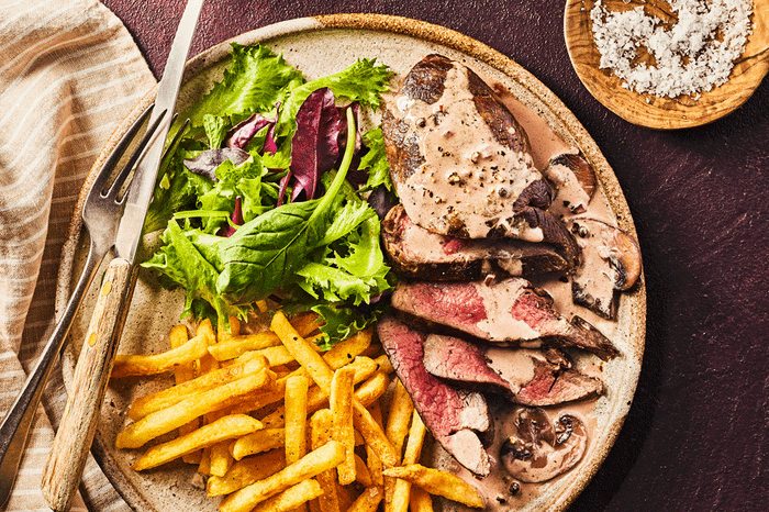 Venison steaks with mushroom peppercorn sauce Slices of venison on a plate with chips, salad and mushroom peppercorn sauce