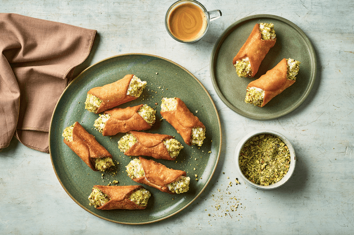 Cannolli A large plate of cannoli on a grey background with a shot of espresso and a small bowl of chopped pistachios