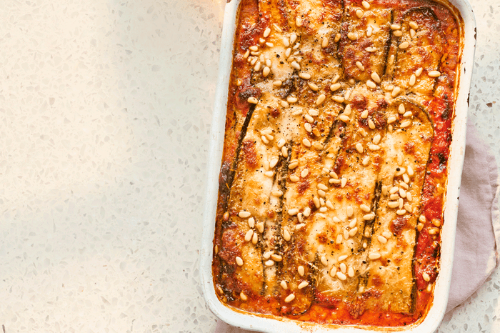 Courgette parmigiana Baking dish with courgette parmigiana topped with toasted pine nuts