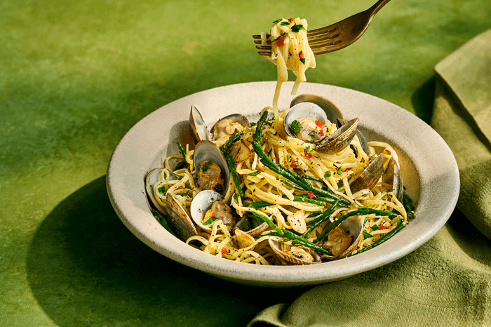 Tagliolini alle vongole Tagliolini alle vongole in a bowl with a fork and a green background