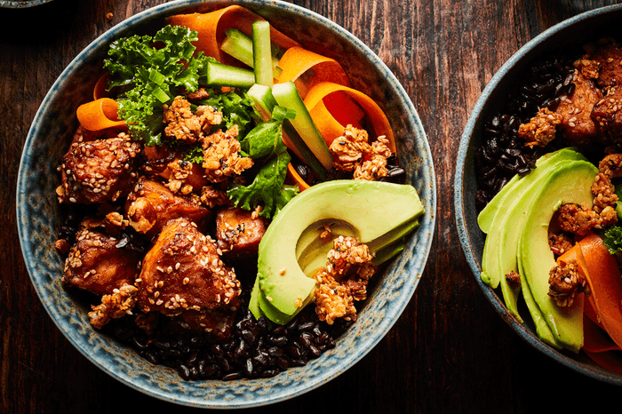 Tempeh rice bowl garnished with avocado, carrot ribbons, cucumber and kale